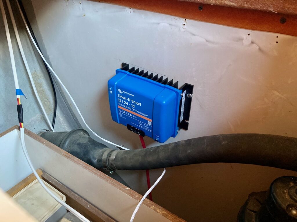 Victron Orion-Tr Smart DC-DC charger mounted on a vertical surface above the exhaust hose and a shelving unit.  Several wires are visible in the frame.  The charger is not yet fully connected to the wires.